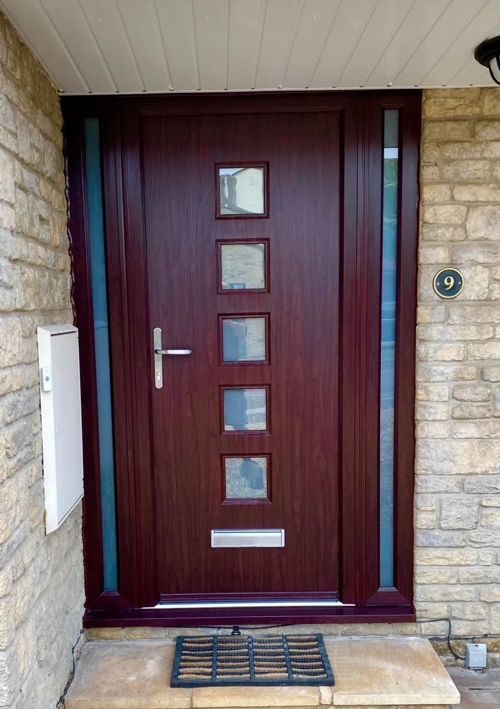 A dark brown wooden front door with five small square glass windows in a vertical line. The door has a silver handle and letterbox. It's set in a stone facade, with a house number 9 to the right and a small doormat at the base.